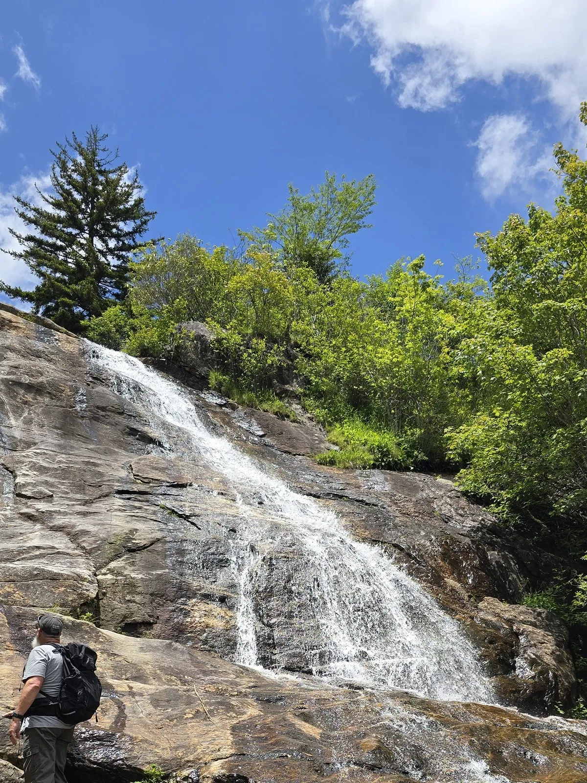 Upper Falls at Graveyard Fields cascading down a granite rock face, a hiker standing at the base for scale
