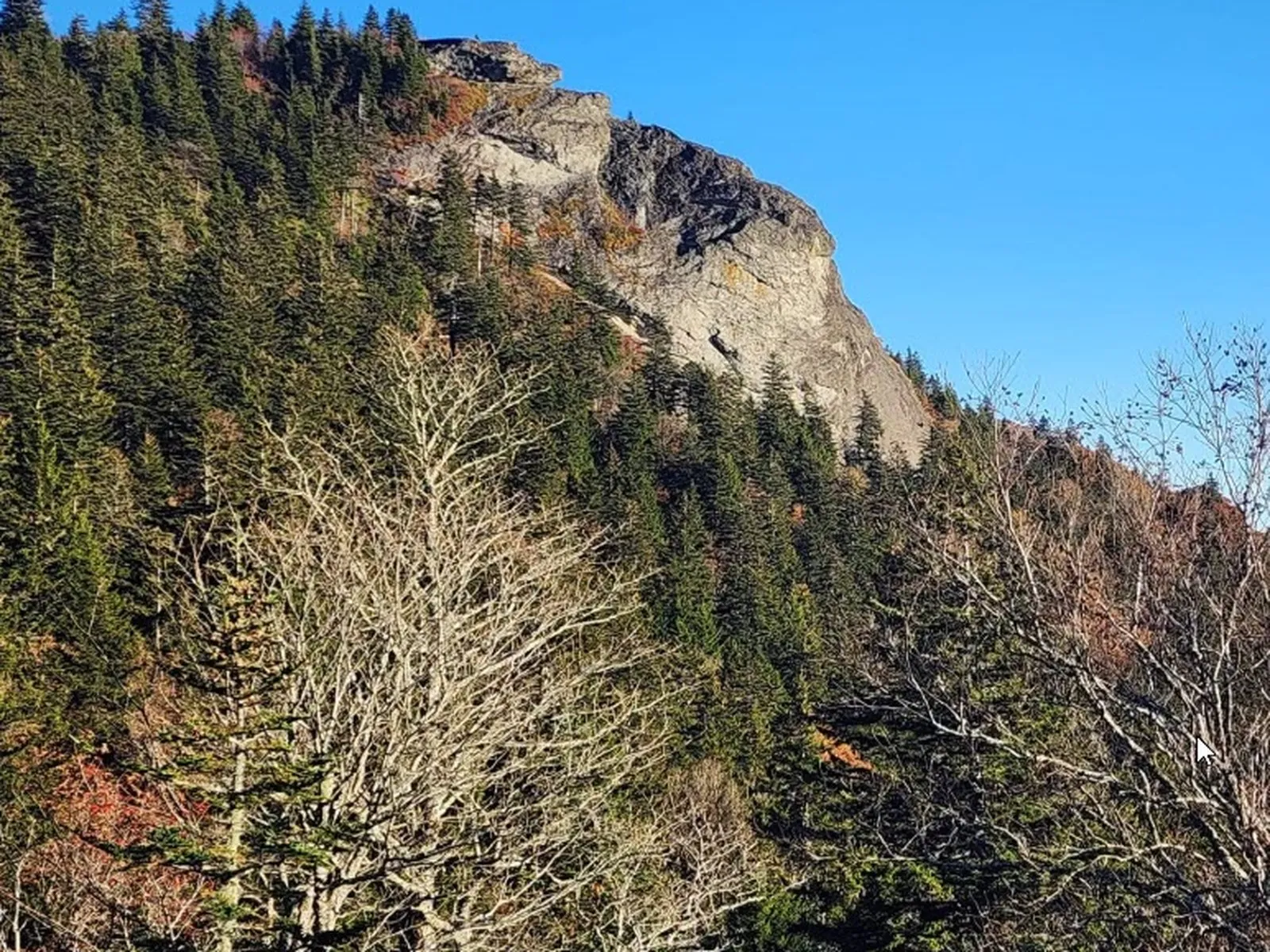 A hiker at the rocky summit of Devil's Courthouse looking out across a 360-degree panorama of layered mountain ridges