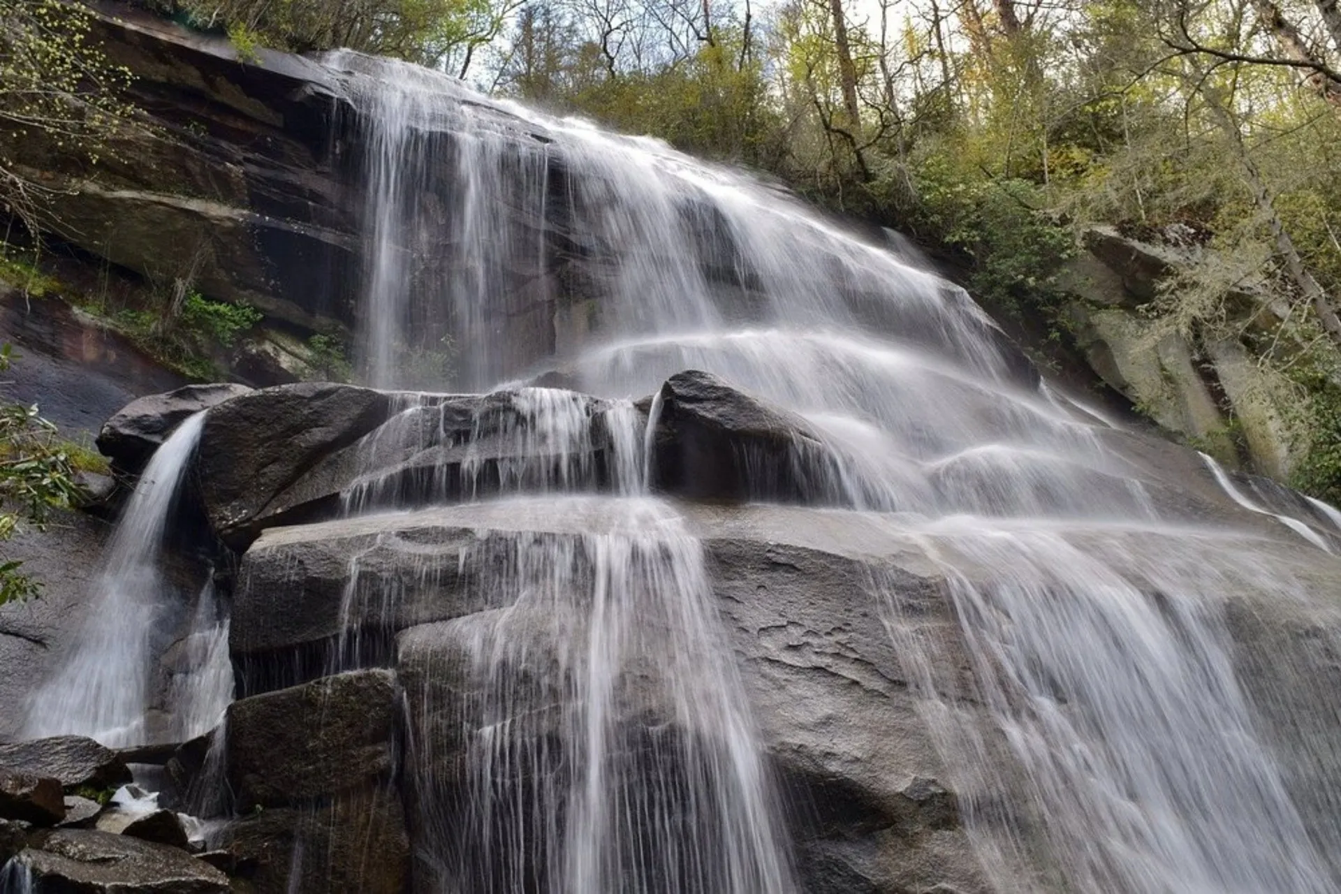 Daniel Ridge Falls tumbling down a broad, tiered rock face surrounded by green Pisgah forest