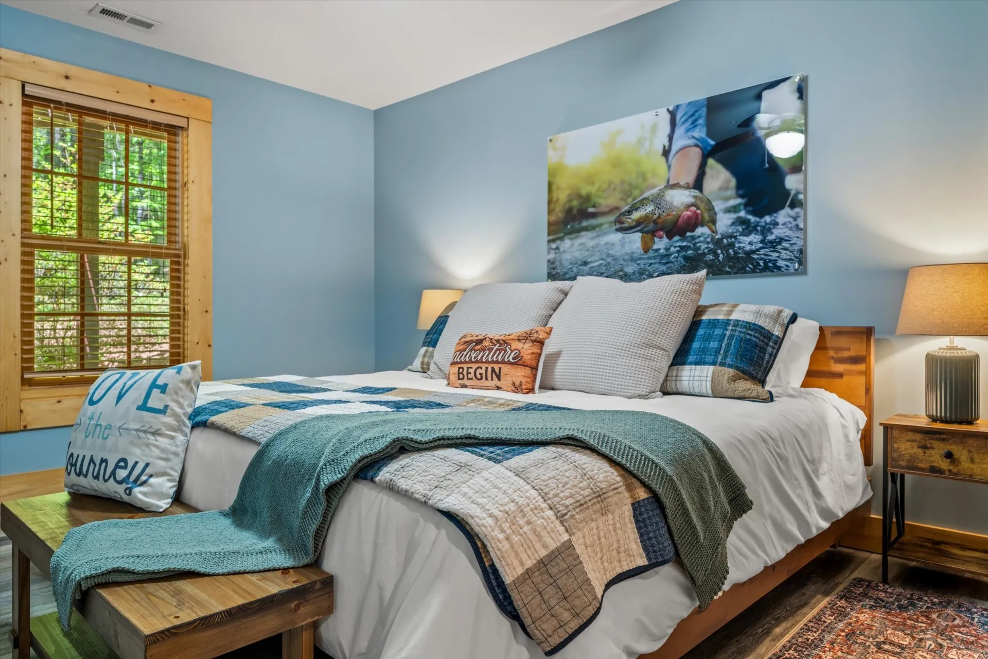 Davidson Room — king bed with blue plaid quilt, fly-fishing trout photography over the headboard, and forest views through the window