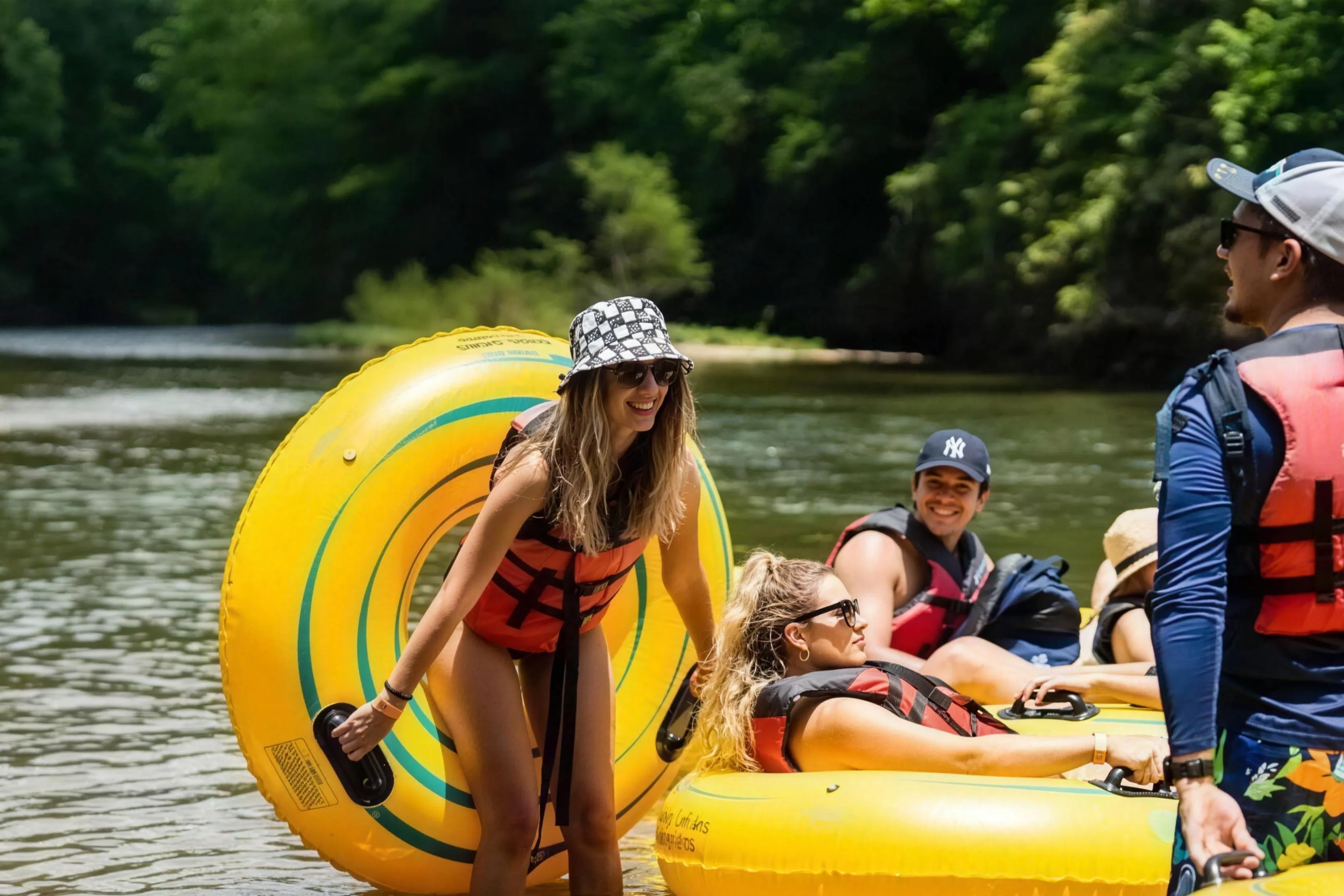 A group of friends laughing and getting their tubes ready on the French Broad River for a summer tubing trip from Headwaters Outfitters