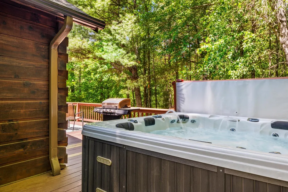 Covered hot tub on the wood deck beside the cabin, with forest views