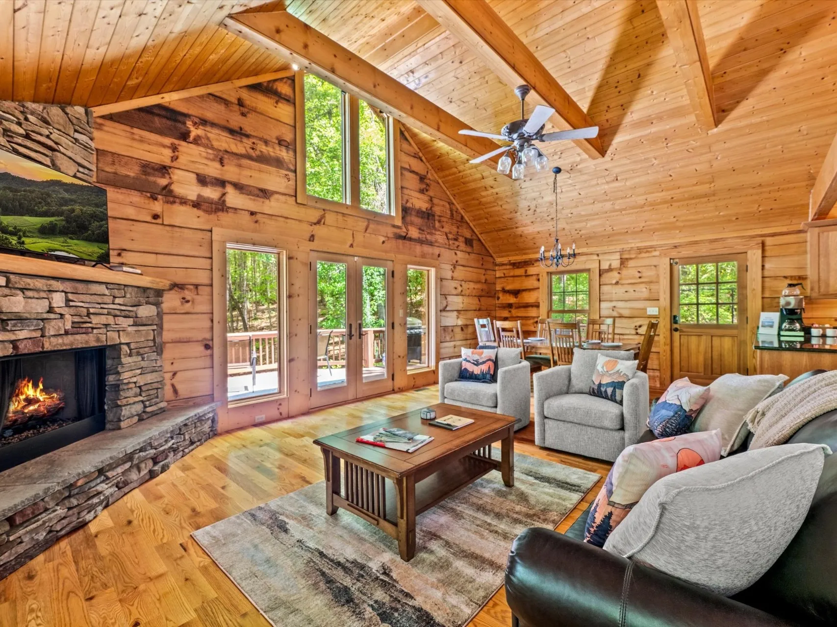 Main living area with stone gas fireplace, vaulted pine ceiling, and french doors opening onto the deck
