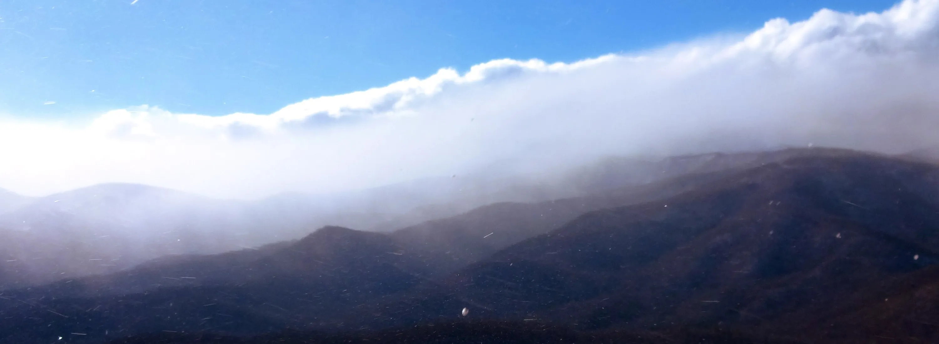 A winter snow squall rolling in white over dark forested ridges under a blue sky, seen from the top of Looking Glass Rock