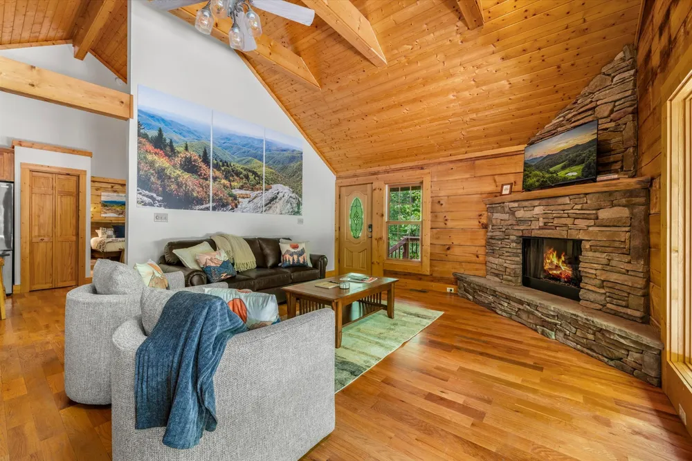 Main living room with stone gas fireplace, vaulted pine ceiling, and french doors to the deck