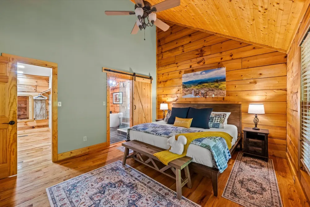 Primary bedroom with king bed, vaulted pine ceiling, and barn-door entry to the soaking-tub bath
