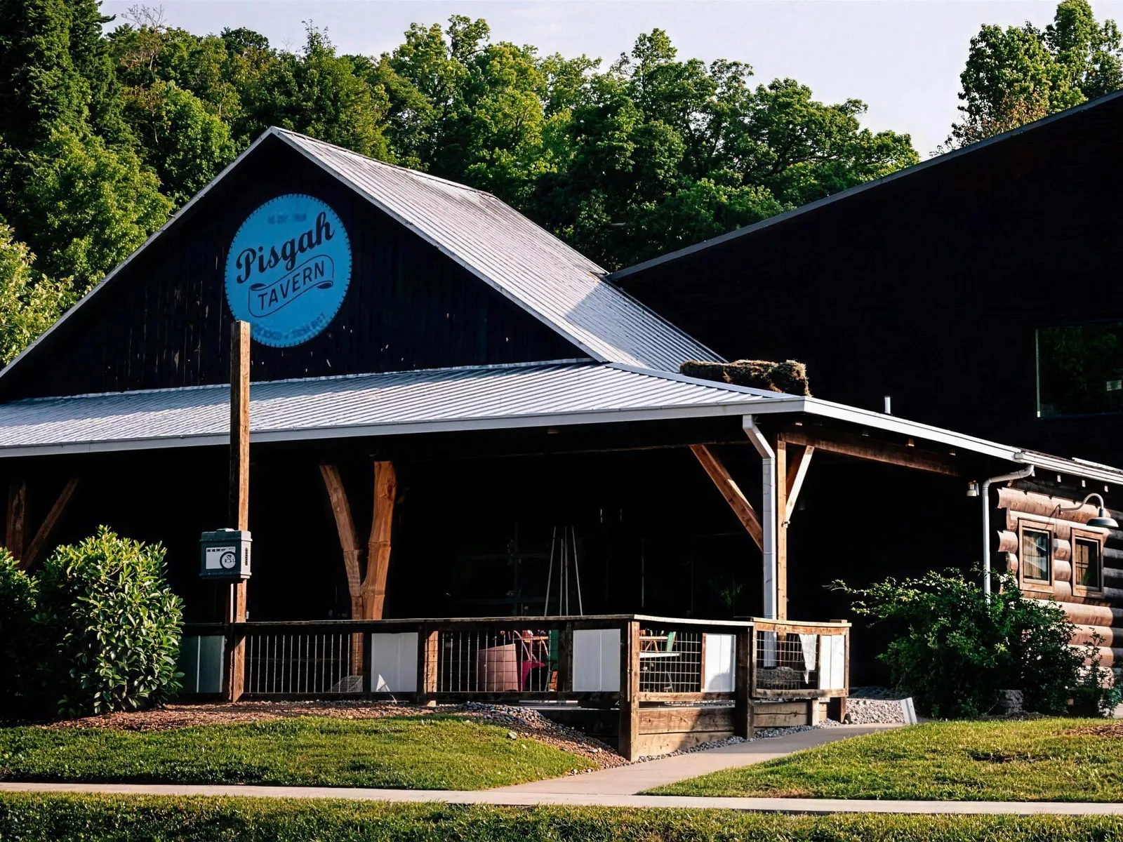 The Pisgah Tavern side of The Hub in Pisgah Forest, NC, with the round blue Pisgah Tavern sign on the gable above a covered wooden porch